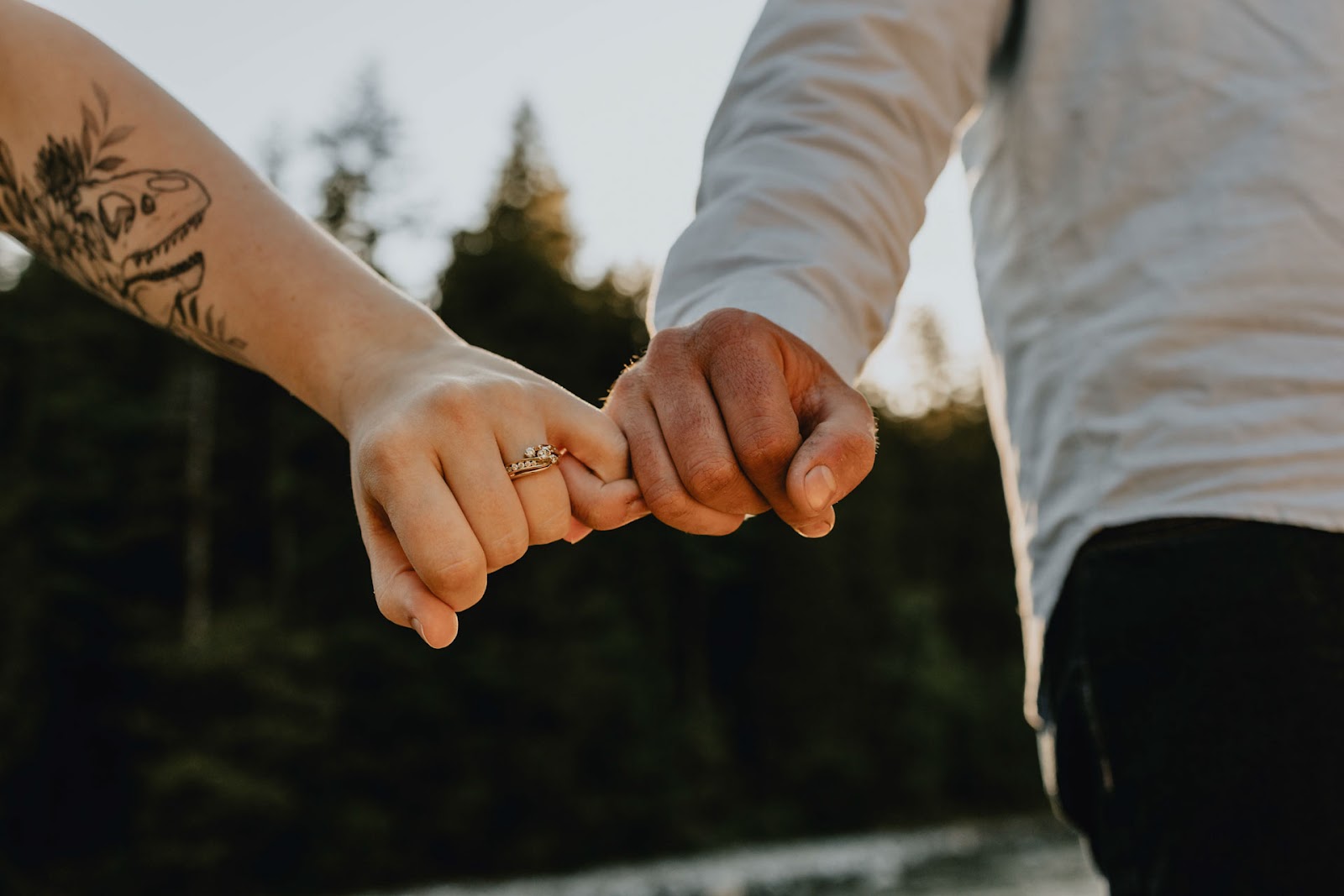 close up photo of couple holding pinky fingers and showing engagement ring